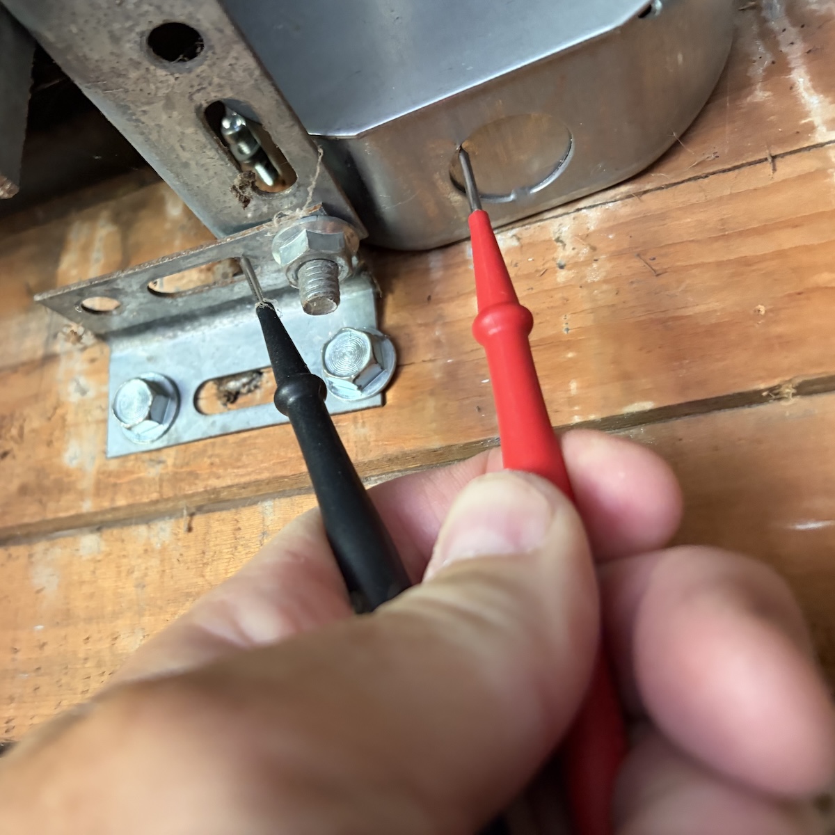 Red and black electicity meter probes touching an exposed metal electrical box and nearby exposed metal
