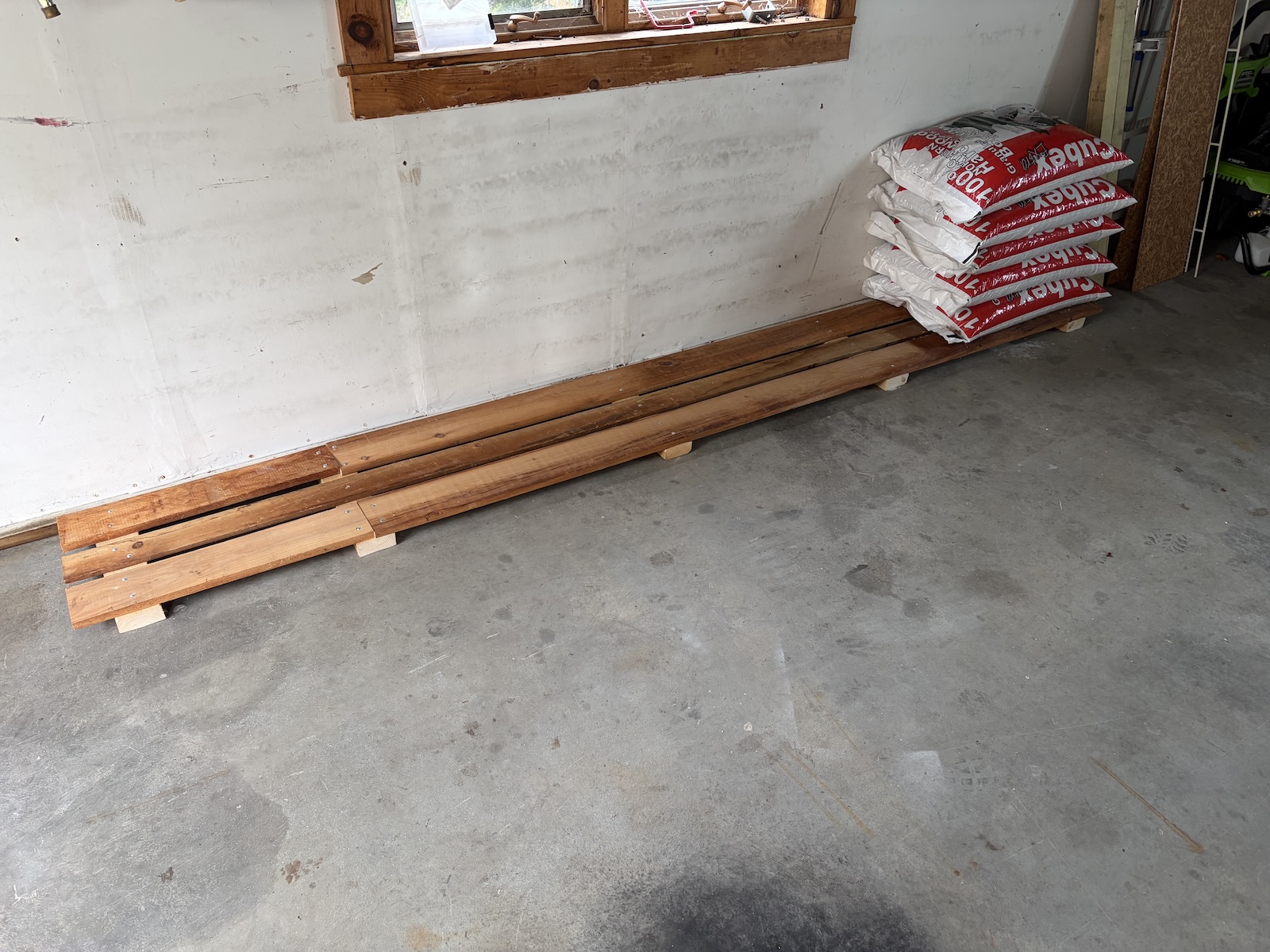 Wooden slats floating over concrete garage floor, some bags of wood pellets on the far end.
