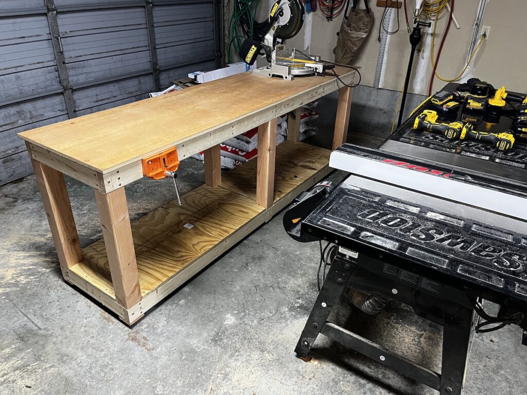 wooden workbench home built in the garage, roll-up door in the background, table saw in the foreground.