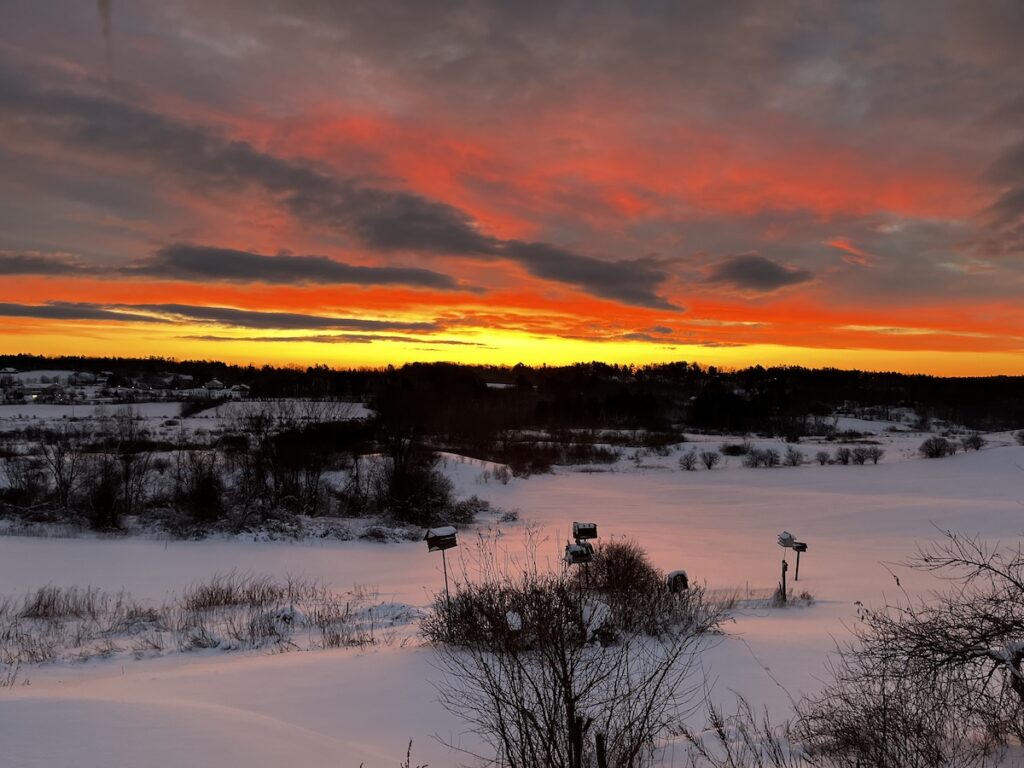 Sunrise in Maine, reds and oranges of the clouds reflecting in the snow on the fields to the east of the house.