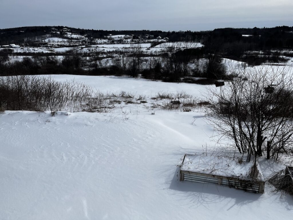 Snow covered landscape view east from our house, planter boxes in foreground, fields and distant ridgeline.